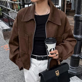 Person wearing a brown jacket holding a coffee cup and black handbag on a street.